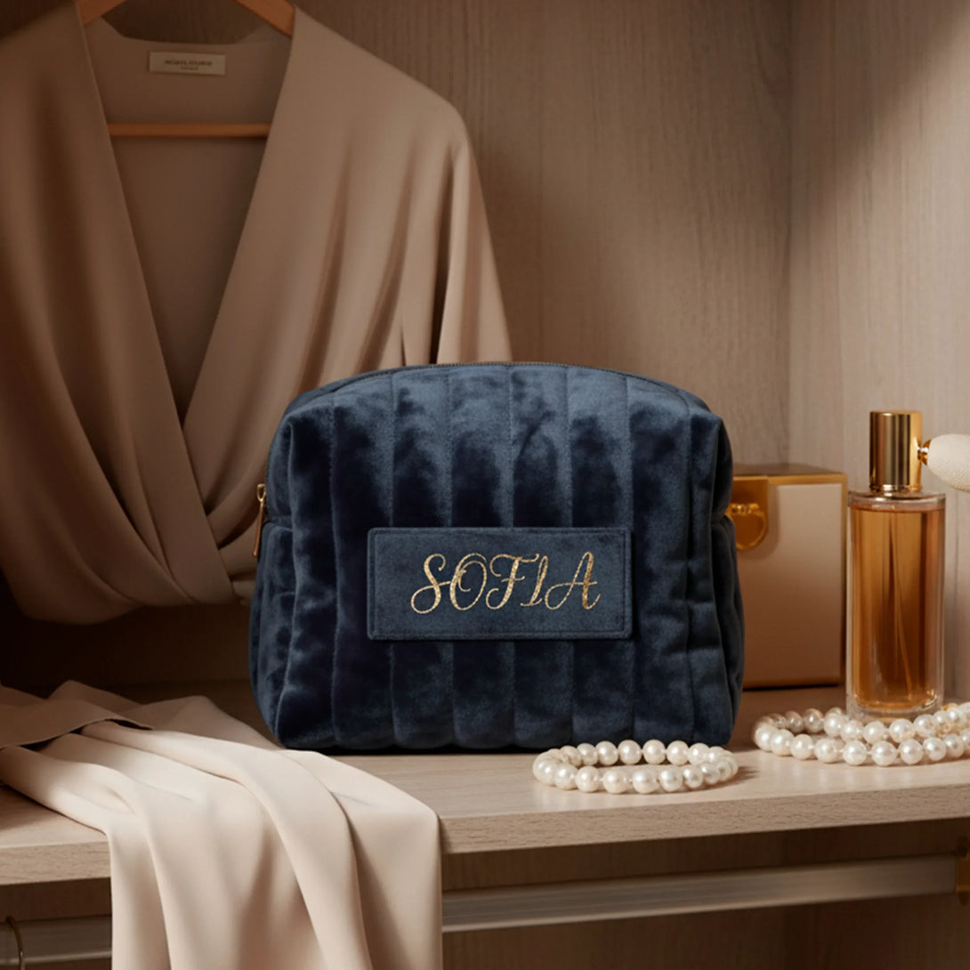 Navy blue personalized velvet pouch with gold embroidery Sofia on wooden shelf with beige scarf, pearls, and perfume